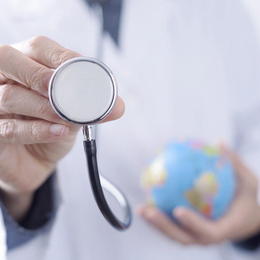 closeup of a young caucasian doctor man with a world globe in one hand and a stethoscope in the other hand